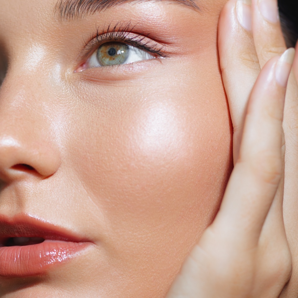 Close-up of a woman touching her face, showcasing radiant skin and a green eye. Perfect for skincare and beauty promotions, high-quality advertisements, and conceptual beauty visuals.