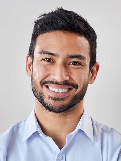 A smiling man with short dark hair and a beard, wearing a light blue collared shirt.