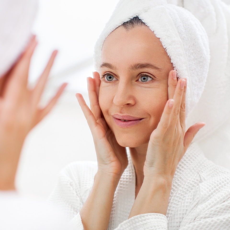 Happy 40s middle aged woman model touching face skin looking in mirror reflection. Smiling adult lady pampering, healthy moisturized skin care, aging beauty, skin care treatment cosmetics concept